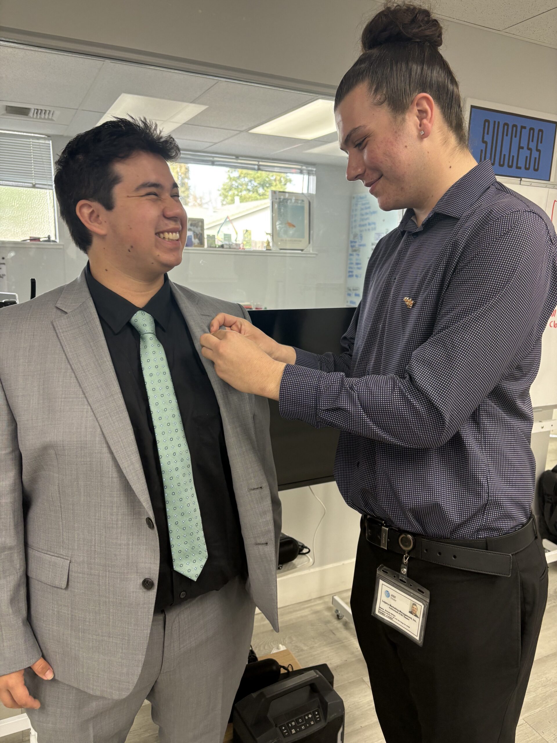 Two team members at Legacy Marketing Management, one of them is helping adjust the other’s pin